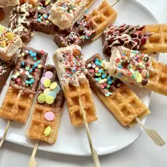 Bunte Waffeln am Stiel, getaucht in Schokolade und bestreut mit Streuseln und bunten Zuckerlinsen, laden zum Naschen ein.