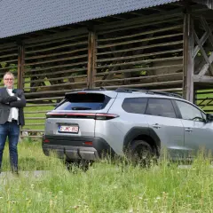 Man i kavaj står bredvid silverfärgad Toyota bz4x under ett gammalt träskjul.