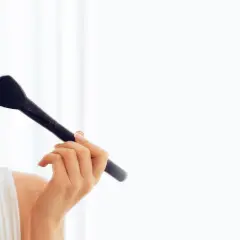 Uśmiechnięta blondynka nakłada puder pędzlem na policzek.