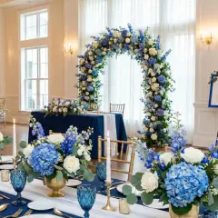 Elegancka sala weselna z niebieskimi akcentami. Kwiatowe łuki i dekoracje stołów tworzą magiczną atmosferę.