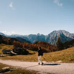 A lone hiker enjoys a scenic autumn day hiking in Bavaria, with colorful trees and majestic mountains in the background.