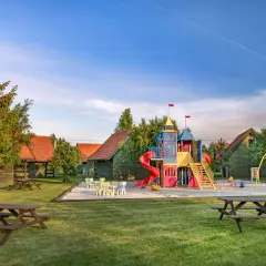 Idealne miejsce na majówkę z dziećmi: kolorowy plac zabaw, domki i zielony trawnik.