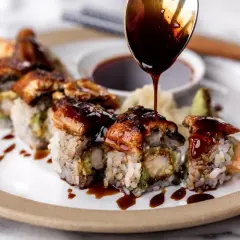 A spoon drizzles rich unagi sauce over a delicious sushi roll, showcasing how to make unagi sauce for a perfect finish.