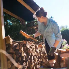 Femme avec des bûches de bois sous un abri.