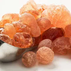 Grains ambrés de gomme arabique dans une cuillère métallique. Qu'est-ce que la gomme arabique ? Une résine naturelle aux multiples usages.