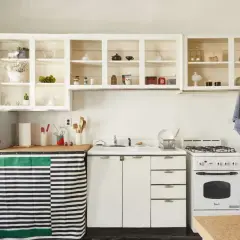 A cozy kitchen with open shelving displaying decorative items. A striped curtain hides the dishwasher, showcasing clever rental friendly upgrades.