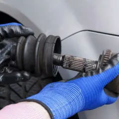 Manos enguantadas sostienen un eje de transmisión con una junta homocinética, parte esencial de las rotulas del coche.