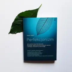 Książka "Perfekcjonizm" Sharon Martin, z liściem w tle, obiecuje uwolnienie od samokrytyki i budowanie wewnętrznej równowagi.