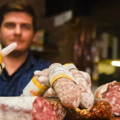 Un hombre con guantes blancos muestra varios tipos de salami, un embutido curado.