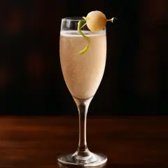Ett elegant drink med bubbel, garnerat med en citronskalsslinga och en rund fruktbit på en cocktailpinne.