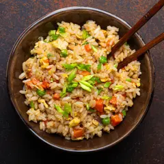 Un piatto fumante di riso alla cantonese ricetta originale, con piselli, carote, uova e cipollotto fresco, pronto per essere gustato con le bacchette.