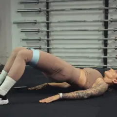 Kobieta wykonuje ćwiczenie glute bridge z taśmą oporową na udach.