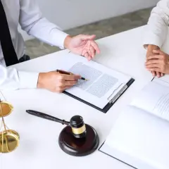 Prawnik omawia z klientem dokumenty, w tym wniosek o przywrócenie terminu. Na stole waga sprawiedliwości i młotek sędziowski.