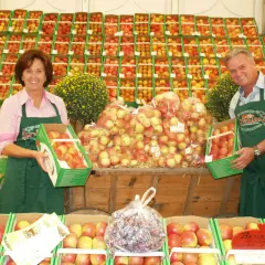 Ein Paar präsentiert Äpfel auf dem markt leichlingen. Sie halten Kisten mit frischen Äpfeln, umgeben von weiteren Obstkisten.