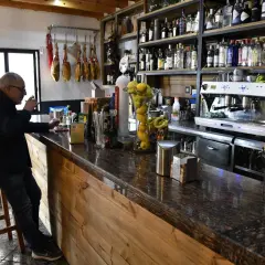 Hombre en taburete en bar Almería Enix, con jamones colgados y estanterías llenas de licores.