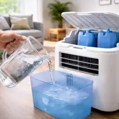 Une main verse de l'eau dans un bac bleu pour un climatiseur mobile. Faut-il mettre de l'eau dans un climatiseur mobile ? Oui, pour le rafraîchissement.