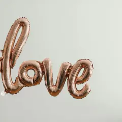 Różowe balony w kształcie napisu "love" unoszą się w powietrzu, symbolizując bezwarunkową miłość do dziecka. Cytaty o tej miłości pasują do tej chwili.