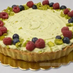 Tarta pistacjowa z białą czekoladą, ozdobiona malinami, borówkami i pistacjami.