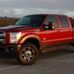 Czerwony Ford F350 King Ranch z brązowym pasem, zaparkowany na tle krajobrazu z wydmami i drewnianym płotem.