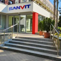 Wejście do sanatorium Sanvit w Ciechocinku. Schody prowadzą do przeszklonych drzwi, a nad nimi widnieje niebiesko-czerwone logo.
