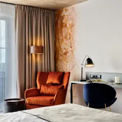 Przytulny pokój w **Bergo Hotel Szklarska Poręba**: pomarańczowy fotel, biurko z lampką i granatowe krzesło.