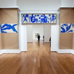 Gallery hallway showcasing Henri Matisse obras: blue cut-outs of figures adorn the walls, with a long horizontal piece above an archway and flowing designs on either side.