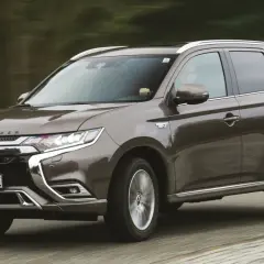 Brązowy Mitsubishi Outlander PHEV jedzie po drodze, z rozmytym tłem lasu.