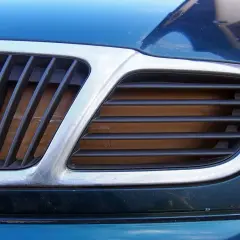 Chromowana osłona chłodnicy w samochodzie, z czarnymi żebrami, chroni silnik przed uszkodzeniami.