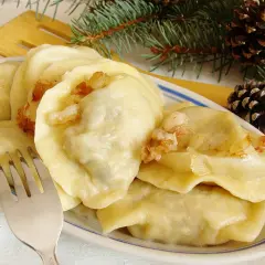 Pyszne pierogi z mięsem i kapustą, okraszone skwarkami, na talerzu z gałązką sosny i szyszkami.
