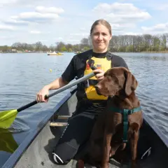 Frau und brauner Hund genießen das Kanufahren mit Hund auf einem sonnigen See.