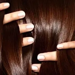Manos peinando un cabello largo y sedoso de color chocolate.