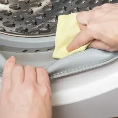 Manos limpian la goma de la lavadora con un paño amarillo para saber como quitar el mal olor de la lavadora.