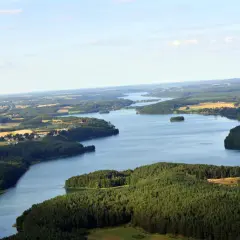 Malowniczy widok na jezioro Raduńskie Dolne otoczone lasami i polami. W oddali widać zabudowania.