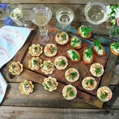 Små, läckra tilltugg till bubbel, serverade på en rustik bricka med blommor och glas. Perfekt för festliga stunder.
