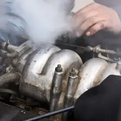 Mechanik próbuje naprawić silnik, z którego wydobywa się gęsty, biały dym.