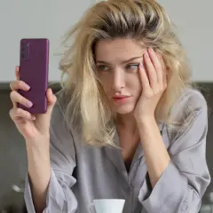 Zmęczona kobieta z telefonem w dłoni, z ręką na twarzy. Czy to objawy uzależnienia od kofeiny?