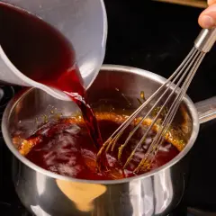 Flüssigkeit wird in einen Topf mit karamellisiertem Zucker gegossen, während ein Schneebesen umrührt, um eine Balsamico-Creme herzustellen.