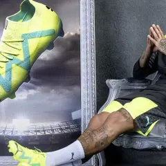 Neymar w neonowych butach piłkarskich na tle stadionu. Buty z technologią Phat Tape idealne na nawierzchnię turf.