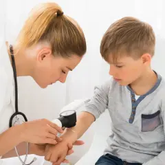 Lekarka bada rękę chłopca dermatoskopem, sprawdzając znamię dysplastyczne.