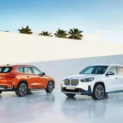 Dos BMW Serie X, uno naranja y otro blanco, posan ante un muro blanco y palmeras.