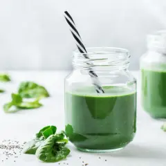 Två glas med grön smoothie, garnerade med spenatblad och chiafrön. Tänk på eventuella spirulina biverkningar innan du dricker.