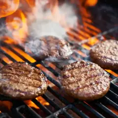 Soczyste burgery z grilla skwierczą na rozżarzonych węglach, otoczone dymem i płomieniami. Idealne na letnie popołudnie.