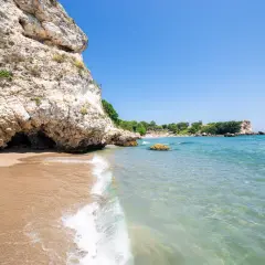 Plaża z piaszczystym brzegiem, skalistym klifem i turkusową wodą Morza Czarnego.