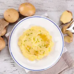 Pyszne puree ziemniaczane na talerzu, obok surowe ziemniaki i obieraczka. Czy cukrzyk może jeść ziemniaki? Tak, w umiarkowanych ilościach!