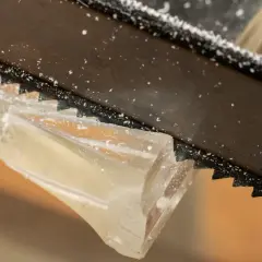 Sågtänder skär genom ett tjockt, genomskinligt material. Små bitar av kapa plexiglas flyger runt.
