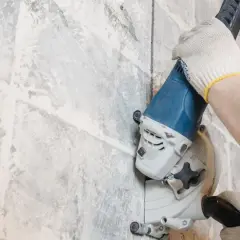 Mani guantate usano una fresatrice per creare un solco nel muro, un metodo per capire se ci sono tubi nascosti.