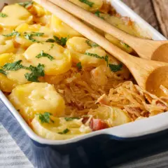 Zapiekanka z ziemniaków i kapusty w naczyniu, ozdobiona natką pietruszki, z drewnianymi łyżkami.