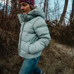 Kobieta w jasnoszarej, puchowej kurtce z kapturem Columbia Puffect Jacket spaceruje po leśnej ścieżce.