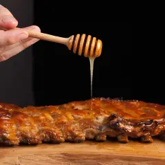 Costillas a la miel jugosas, bañadas con miel dorada de un palillo de madera. Acompañadas de tomates asados.