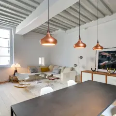 Lámparas colgantes de cobre y un diseño moderno reflejan las **últimas tendencias iluminación salones**. Un sofá blanco y una mesa de comedor completan el espacio.